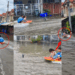 Children Ride Plastic Raft as Motorbike Tows Them Through Flooded Neighbourhood